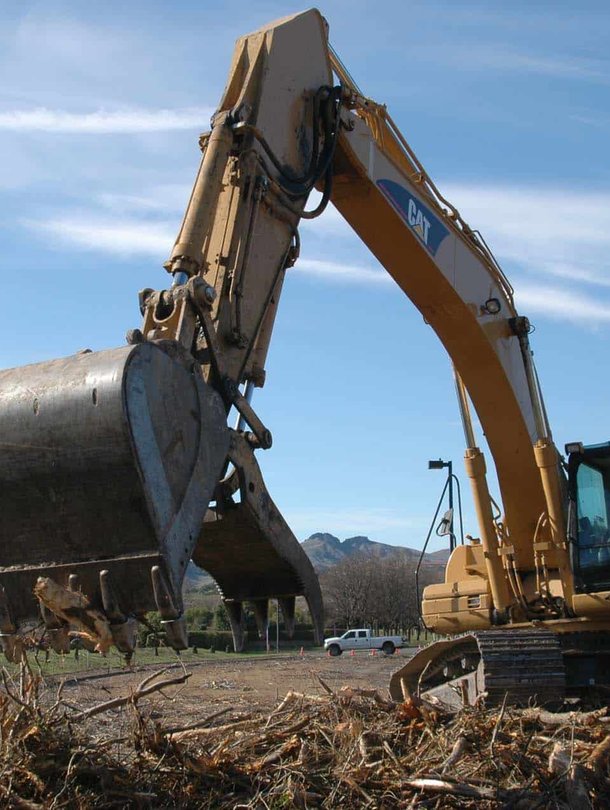 CAT excavator bucket filled with tree debris on sunny day