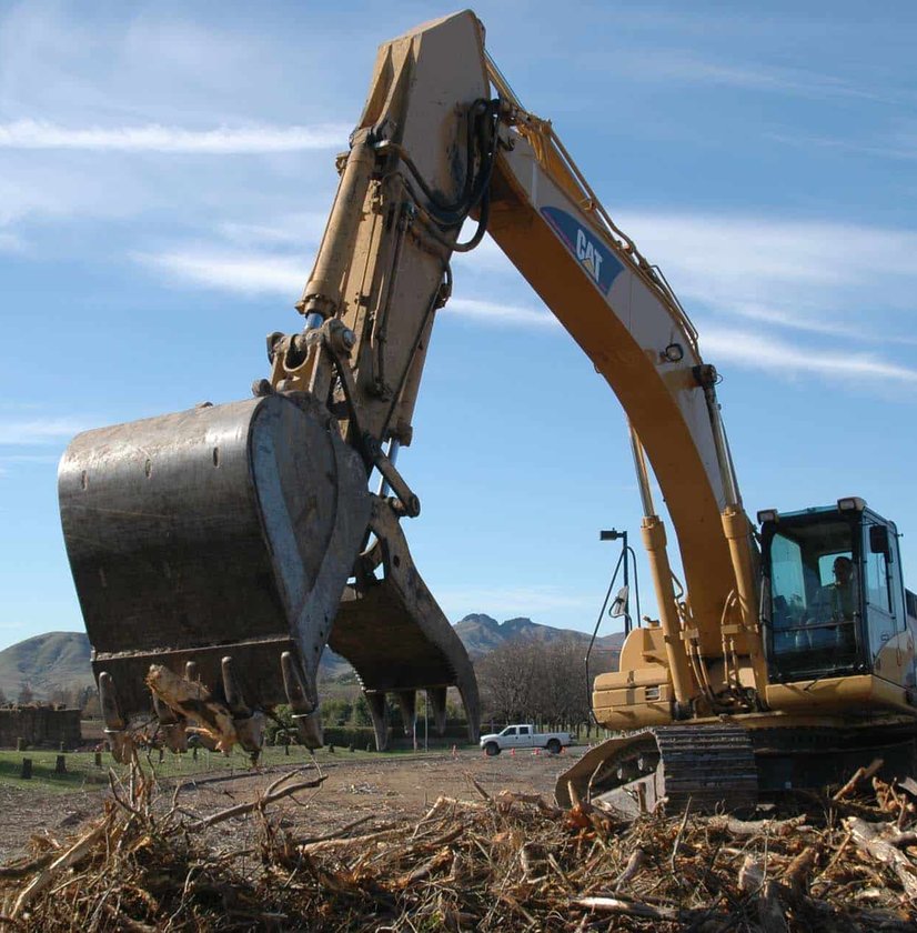 CAT excavator bucket filled with tree debris on sunny day