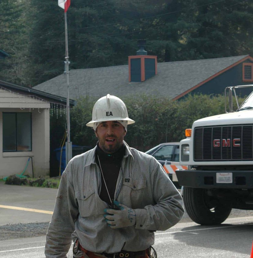 Tree service worker in white hardhat standing beside GMC truck