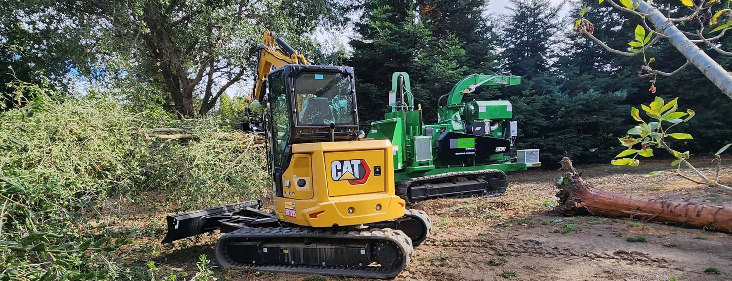 Yellow CAT excavator and green wood chipper on tree removal job site